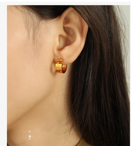 Detail of wide gold hoop earring with star motifs and zircon studs on ear