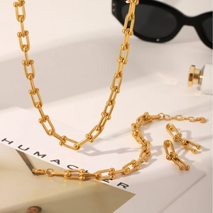 Gouden U-vormige hoefijzer schakel sieradenset met ketting en armband op een modieus bureau