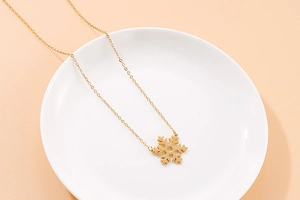 Detailed view of a gold snowflake pendant necklace on a clean white display plate