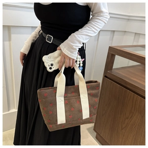 Detail of brown corduroy tote bag with red strawberry patterns and beige handles