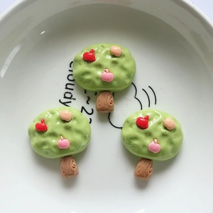 Detailed view of three cartoon apple tree resin charms on a white ceramic plate