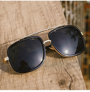 Close-up of black square oversized sunglasses with gold metal bar on wood surface