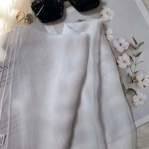 Flat lay of white translucent silk-feel scarf with pearls and fashion accessories