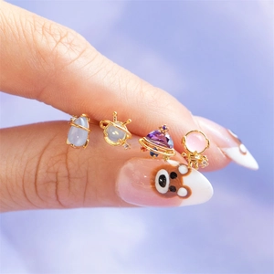 Macro shot of space-themed earrings with colorful crystals held on a fingertip