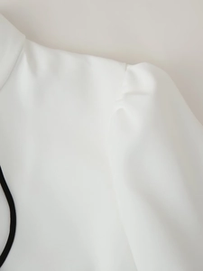 Dettaglio spalla di un abito bianco con maniche a sbuffo e bordi neri a contrasto