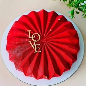 Détail du gâteau géométrique rouge avec décoration LOVE dorée et feuilles d'or fines