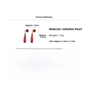 Detailed view of 18k gold plated drop earrings with red pearl beads and silver needles