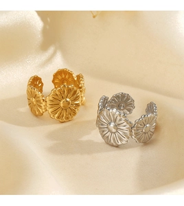 Detailed view of daisy-shaped open rings in gold and silver on soft satin fabric