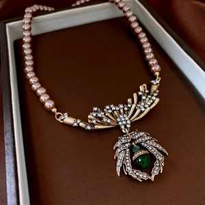 Close-up of vintage necklace with pink pearls, emerald green gem and leaf pendant