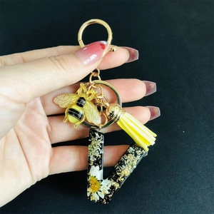 Hand holding resin letter U keychain with white flowers, gold foil, and yellow tassel