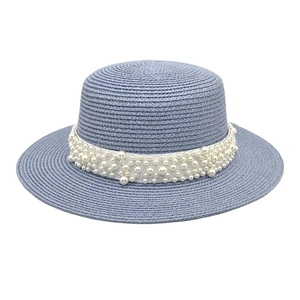 Détail d'un chapeau de soleil bleu clair en paille avec des perles blanches sur un ruban