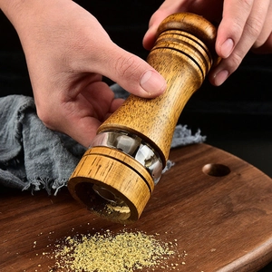Manual oak and glass pepper grinder with ceramic core being used over a wooden board