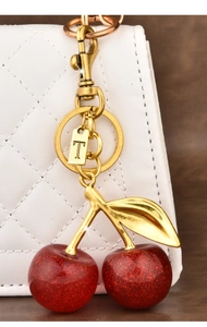 Detail of red glitter cherry keychain with gold letter T tag on a white quilted bag