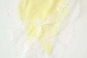Detail of yellow satin dress featuring delicate white eyelash lace trim and silk texture