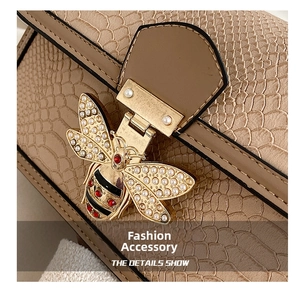 Close-up of beige snake-embossed leather handbag with pearl-encrusted bee metal clasp