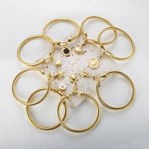 Collection of gold twisted wire bracelets with heart, shell, and coin pendants on stone