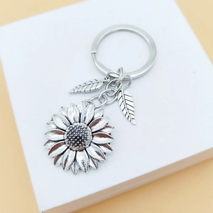 Silver metal sunflower and leaf keychain pendant on a white gift box surface