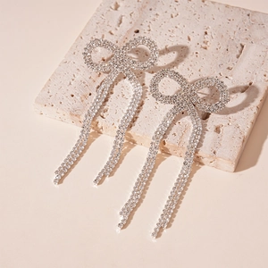 Détail de boucles d'oreilles nœuds argentées avec cristaux sur marbre blanc