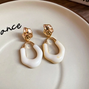 Detailed shot of gold metal studs with white resin drop pendants on a ceramic plate