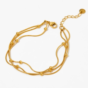 Détail d'un bracelet multicouche doré avec perles, chaîne serpent et fermoir homard