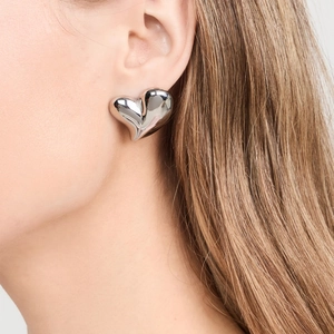 Close-up of a silver heart-shaped stainless steel stud earring on a female model's ear