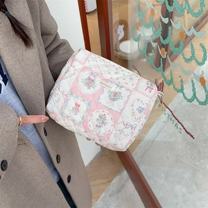 Trousse à maquillage matelassée à fleurs et carreaux roses tenue devant une porte vitrée