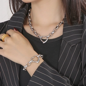 Detail of silver heart necklace and bracelet set with gold ring on model in suit