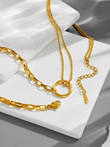 Dettaglio di una collana a strati in acciaio al titanio dorato con ciondolo tondo e moschettone