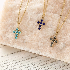 Minimalist stainless steel cross necklaces with blue and black gemstones on a stone base