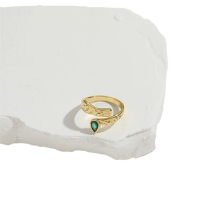 Golden snake ring with green teardrop gemstone on white stone slab, cross grid mesh design