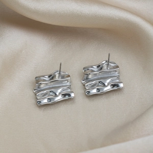 Detailed view of silver irregular wavy square stud earrings on beige silk fabric