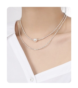 Detail of a layered S925 silver necklace with a white pearl on a model's collarbone