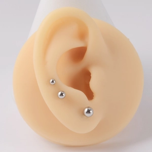 Gros plan de trois boucles d'oreilles boules en acier argenté de tailles variées sur oreille