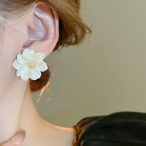 Elegant white resin flower stud earrings with golden pistil worn by a female model