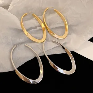 Exaggerated oval hoop earrings in polished gold and silver finish with twisted texture