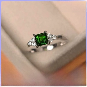 Macro detail of silver ring featuring a green square emerald-cut stone and side diamonds