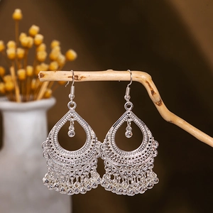 Detail of silver hollow teardrop earrings with peacock bell fringe in boho style