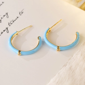 Blue enamel C-shaped earrings with gold plating and diamond accents on a decorative card