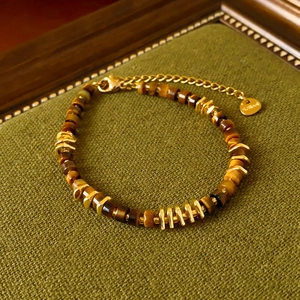 Detail of tiger eye beaded bracelet with golden spacers on dark green texture