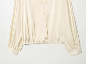 Détail du chemisier en satin champagne avec col en V croisé et ourlet de taille élastique