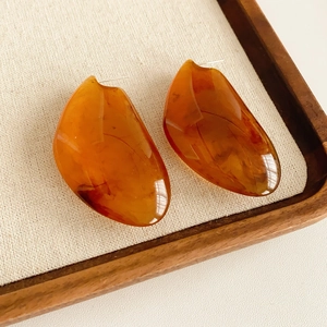Détail de boucles d'oreilles géométriques en résine ambre sur un tissu texturé doux