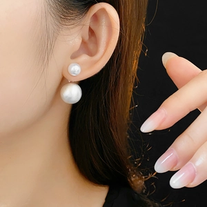 Close-up of elegant double-sided pearl earrings worn by a model against black background