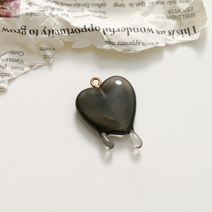 Close-up of translucent dark grey heart charm with teardrop drips on white surface