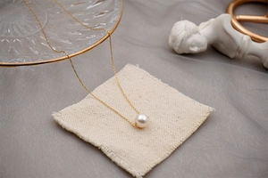 Detailed view of a single pearl pendant on a gold thin chain against grey fabric background