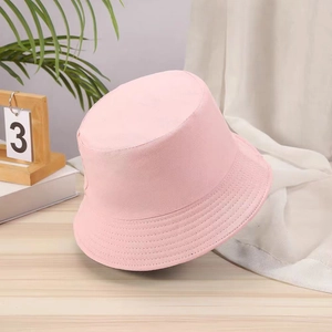 Pink cotton bucket hat shown on a wooden table with soft sunlight and home decor