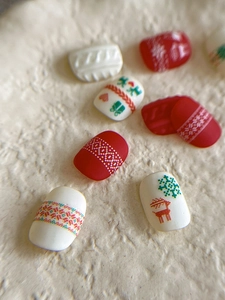 Macro detail of Christmas press-on nails featuring red 3D reindeer and white snowflake motifs