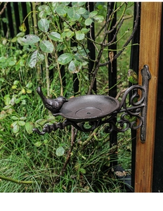 Detailed view of vintage cast iron bird feeder with ornate scrollwork mounted on a post