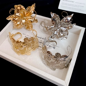 Detail view of bold metallic flower arm cuff in gold and silver finishes on white tray