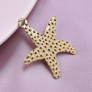 Macro shot of gold starfish pendant with textured finish on soft pink fabric
