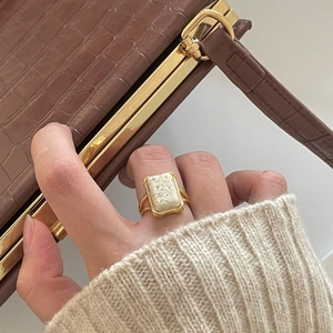 Retro gold ring with rectangular white stone shown on a hand with luxury bag